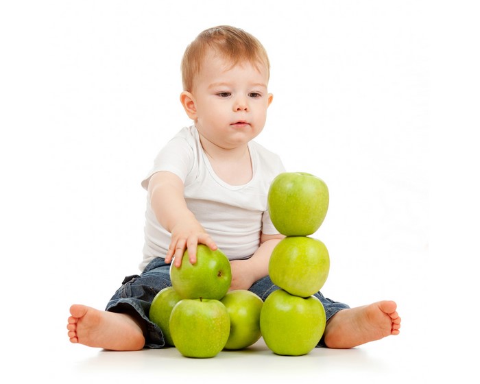 Baby boy playing with green apples on white background