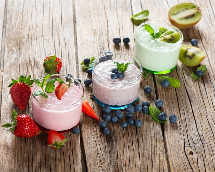 Three yogurts with strawberries, blueberries, and kiwi on wood planks