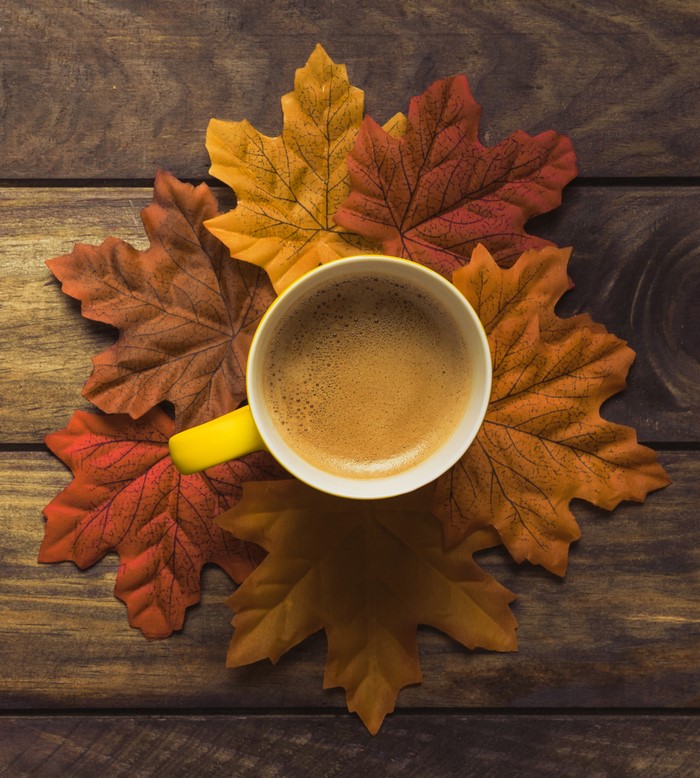 Coffee cup on autumn leaves on wooden table