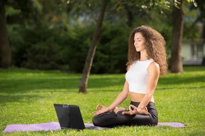Woman meditating in lotus position with laptop