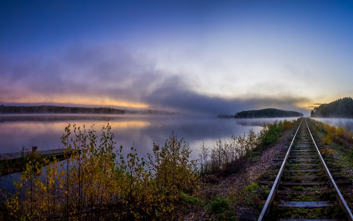 Train tracks by a misty lake at sunrise in autumn