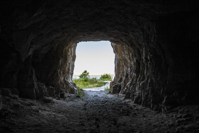 View from inside a dark cave looking out to a bright landscape
