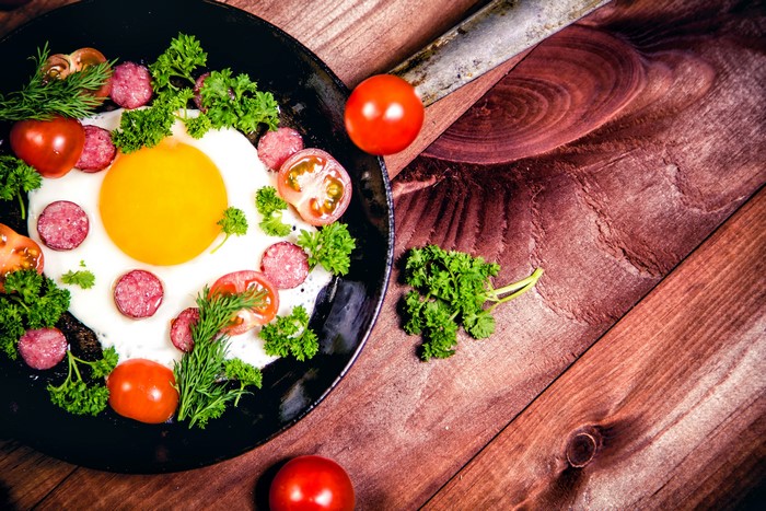 Fried egg with sausage and tomatoes on wood planks