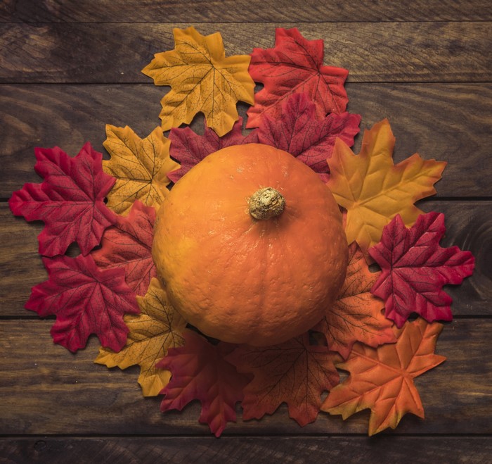 Pumpkin surrounded by autumn leaves on wooden background