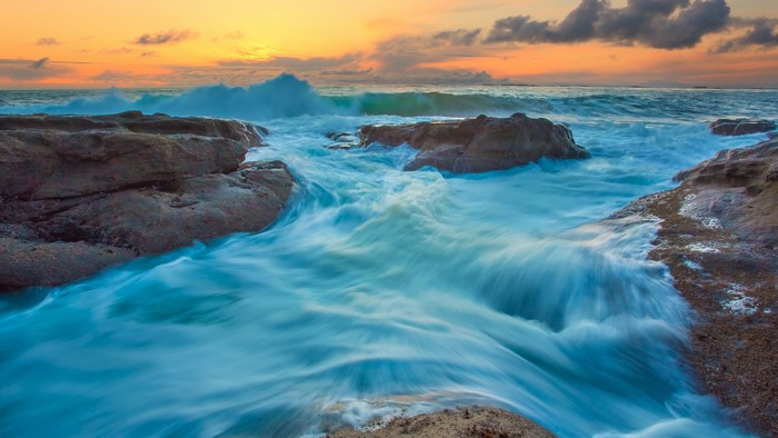 Ocean waves crashing on rocks at sunset