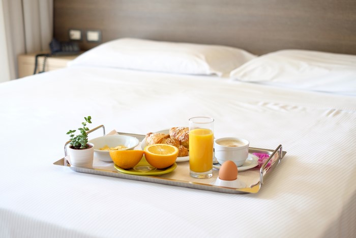 Breakfast tray with juice, coffee, eggs, and croissants on a bed