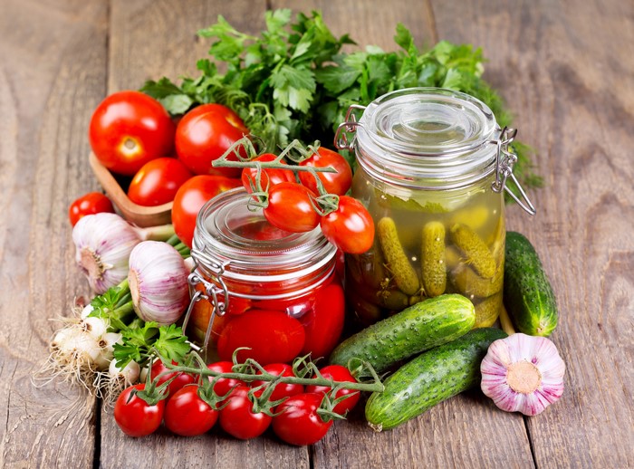 Tomatoes, Cucumbers, Garlic, and Pickles in Jars on Wood