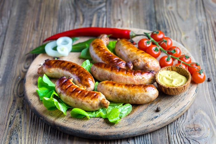 Grilled sausages with tomatoes and mustard on a wooden board