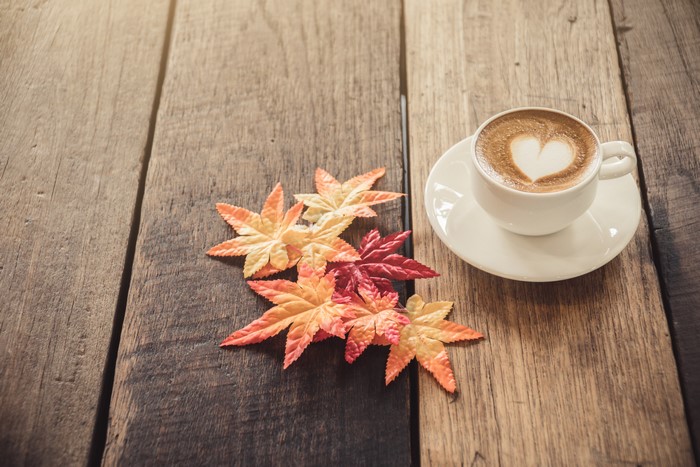 Cappuccino with heart art and autumn leaves on wood