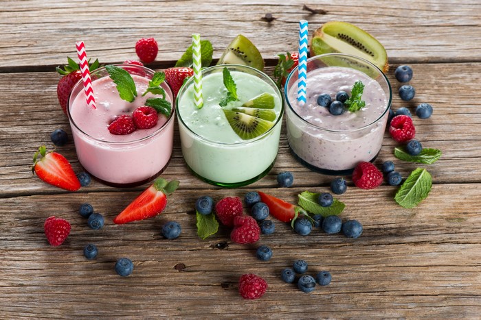 Three fruit smoothies with berries and kiwi on wood