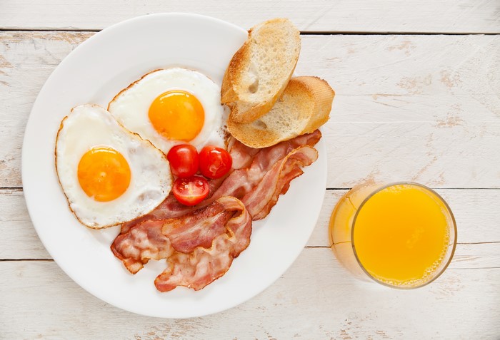 Fried eggs, bacon, tomatoes, bread, and orange juice on a plate