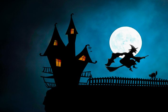 Silhouette of a witch flying past a haunted castle under the moon