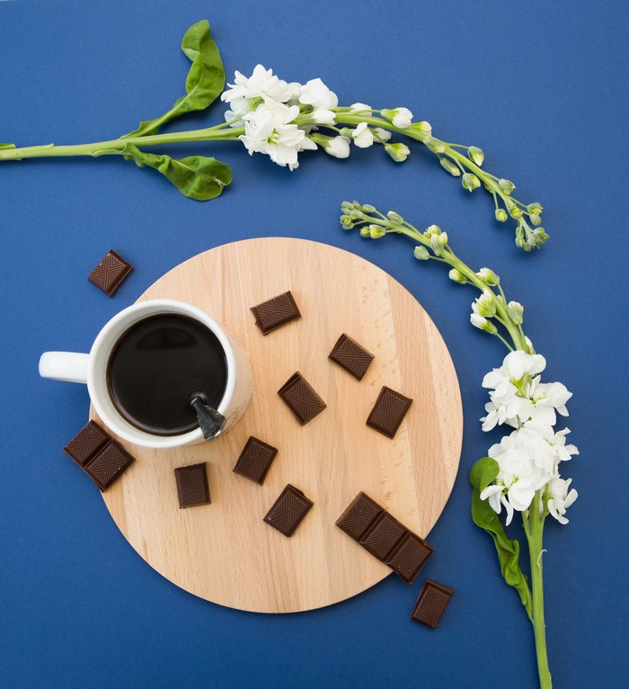 Coffee cup with chocolate and white flowers on blue background
