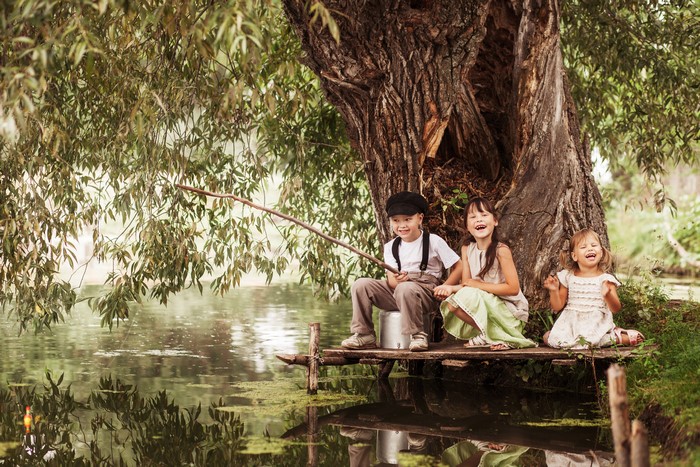 Three children fishing by a large tree