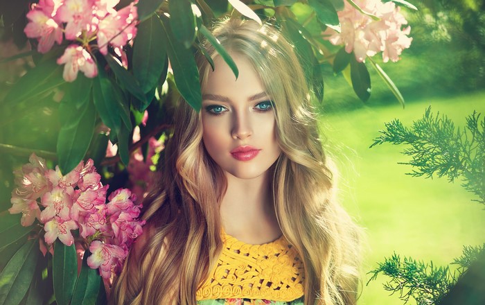 Blonde girl with blue eyes among pink Rhododendrons