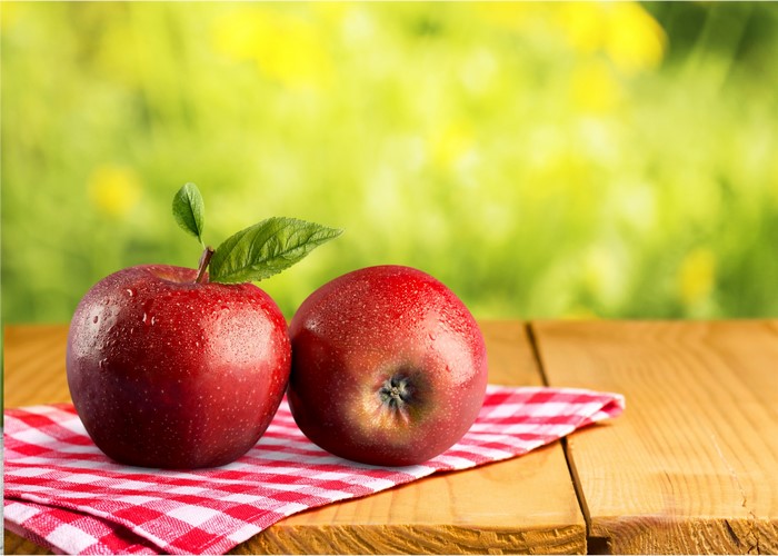 Two red apples on a wooden table with a checkered cloth