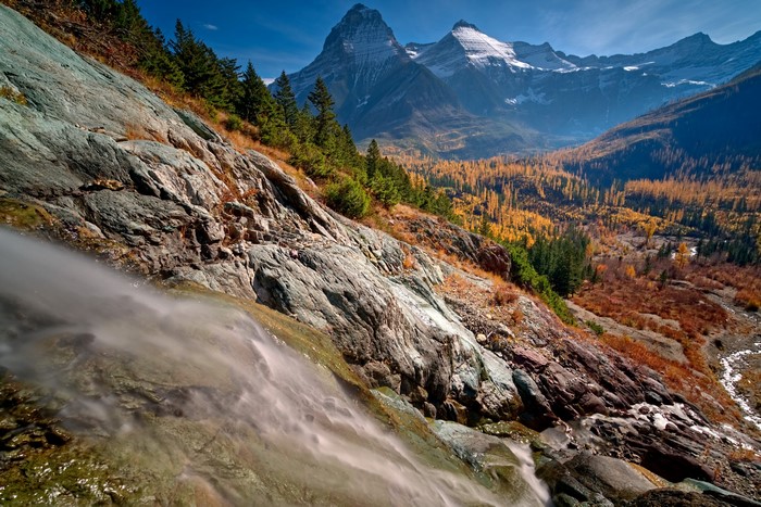 Waterfall cascading down rocky slope with autumn mountains in background