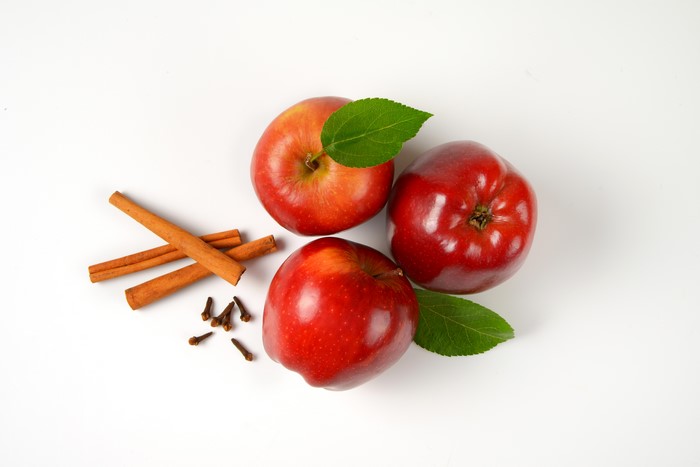 Three red apples with cinnamon sticks and cloves on white background