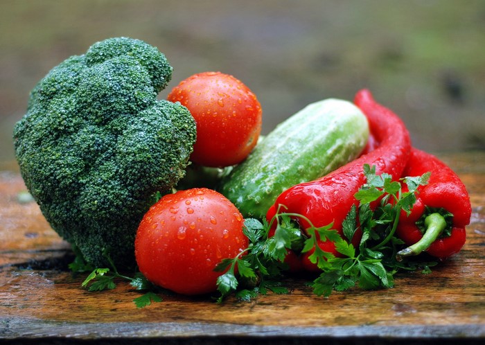 Broccoli, tomatoes, cucumber, bell peppers, and parsley on a wooden surface