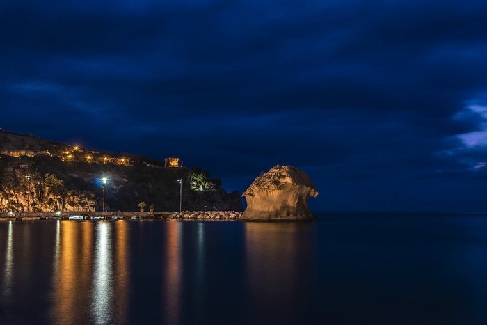 Night view of a rocky coast with lights and a sea stack