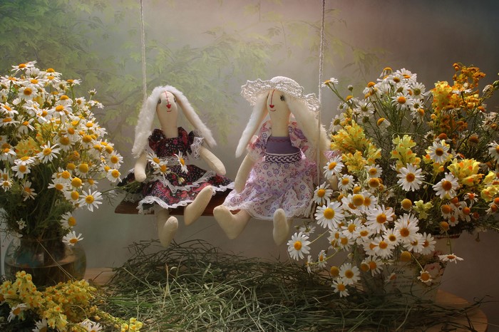 Two bunny dolls on a swing with flowers