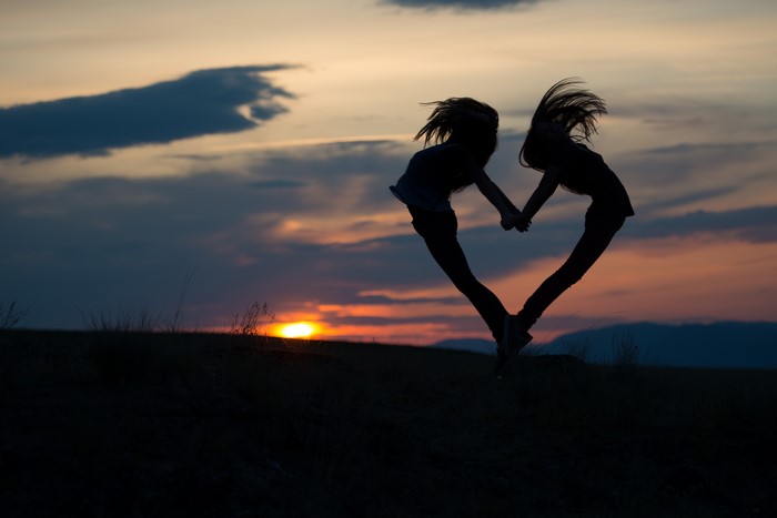 Two people forming a heart silhouette at sunset