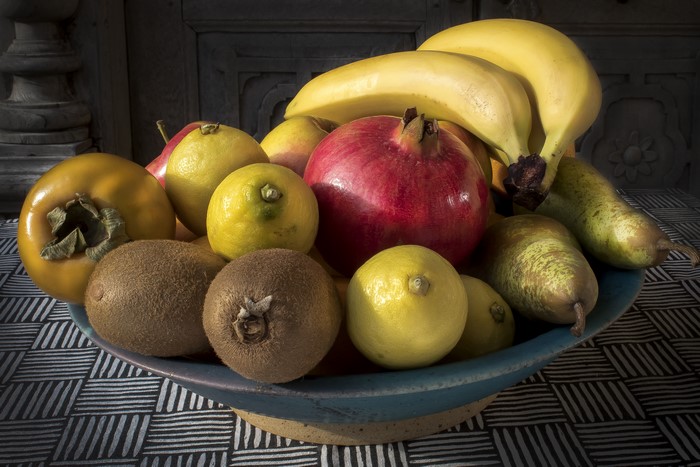 Fruit bowl with bananas, pomegranate, lemons, persimmon, kiwi, and pears