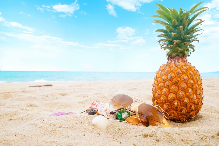Pineapple and sunglasses on a sandy beach