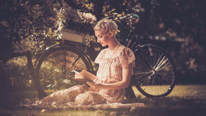 Blonde girl reading a book by a bicycle