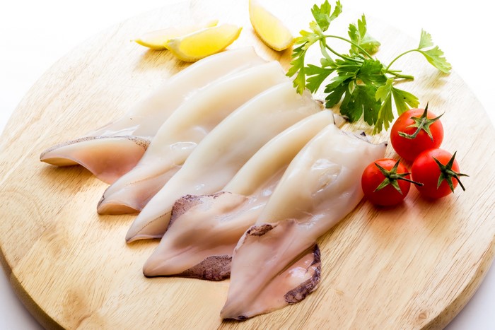 Raw squid on a wooden cutting board with tomatoes and lemon