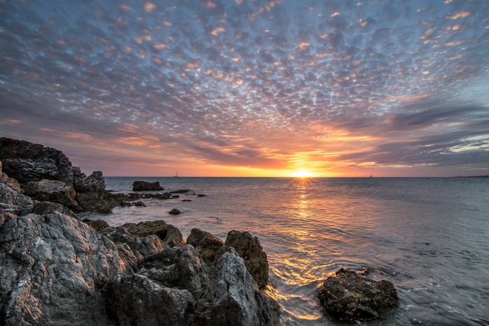 Sunset over the sea with rocky shore and sailboat