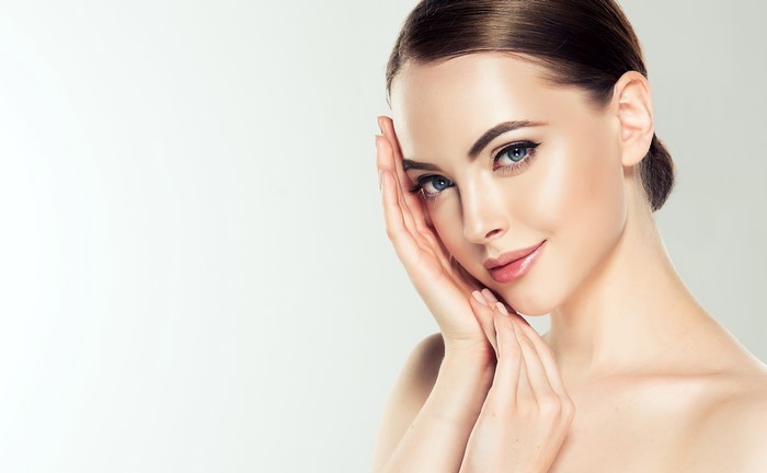 Woman with brown hair and blue eyes, hands on face