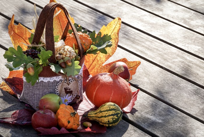 Autumn harvest basket with pumpkins and apples on wood planks