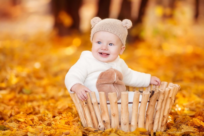 Baby in a bear hat sitting in a basket in autumn leaves