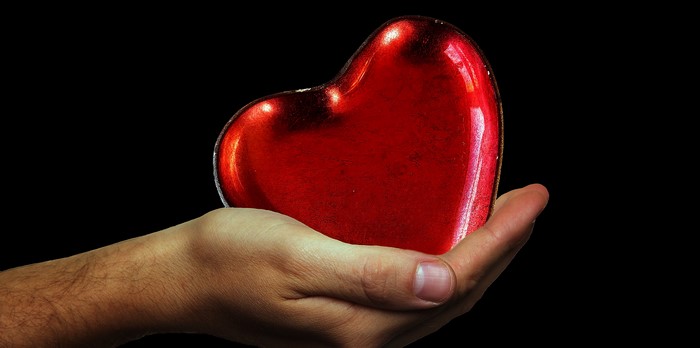 Hand holding a red heart on black background