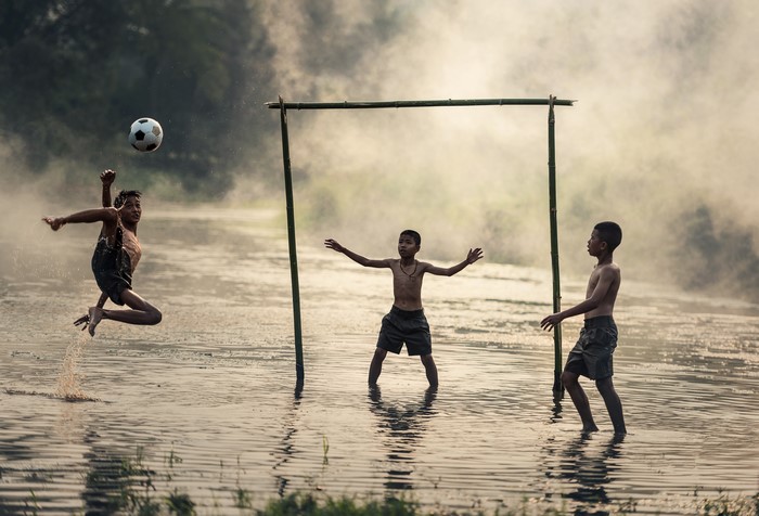 Boys playing soccer in water with fog