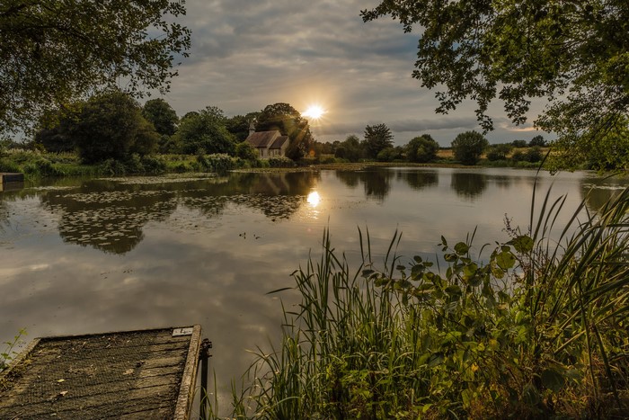 Sunset over a lake with a small house and a wooden dock