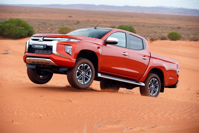 Red Mitsubishi Triton pickup truck driving on sand dunes
