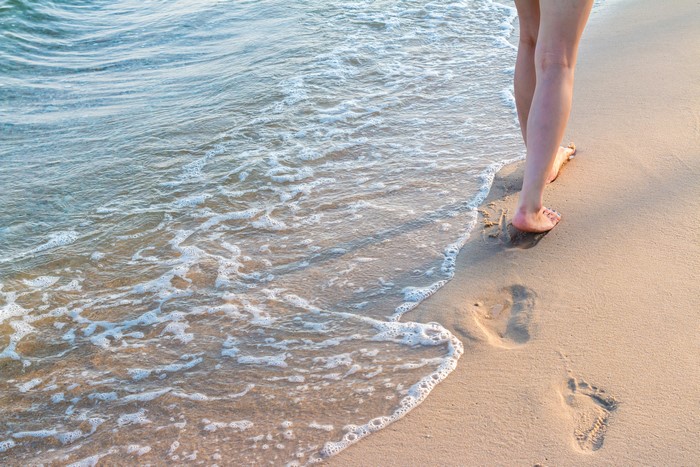 Legs walking on beach with footprints