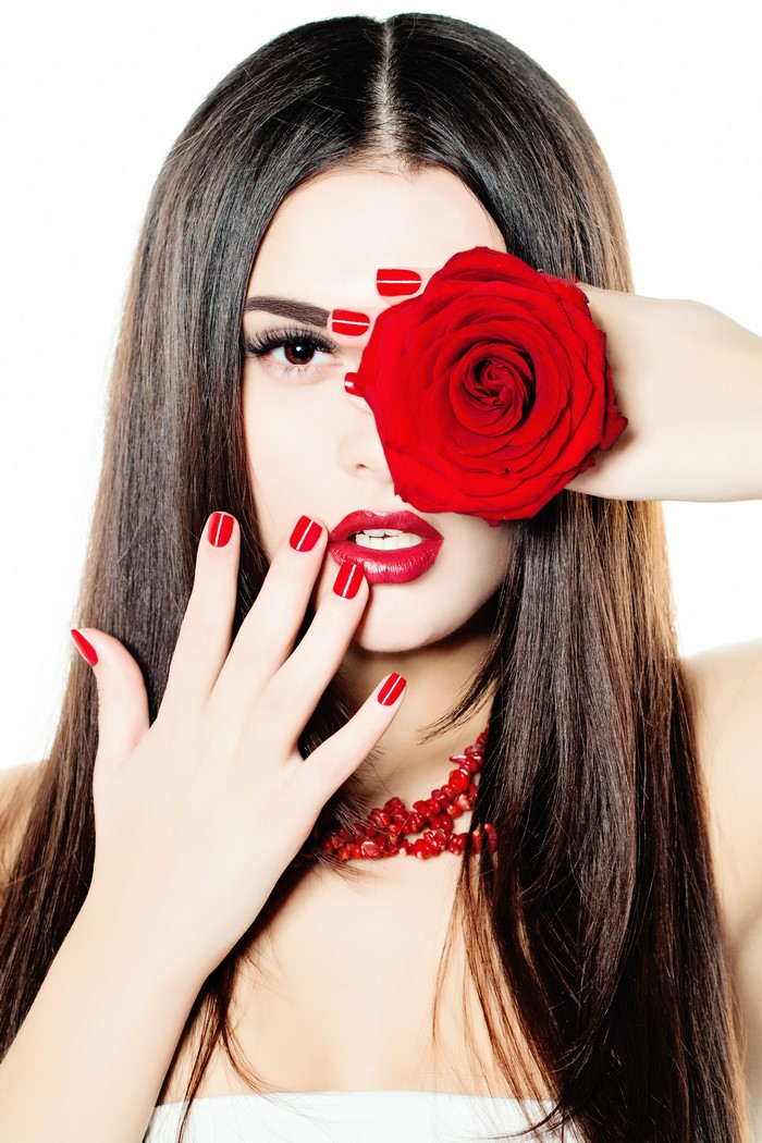 Woman with red rose covering eye and red manicure