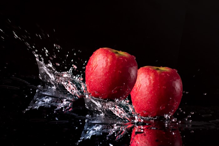 Two red apples with water splash on black background