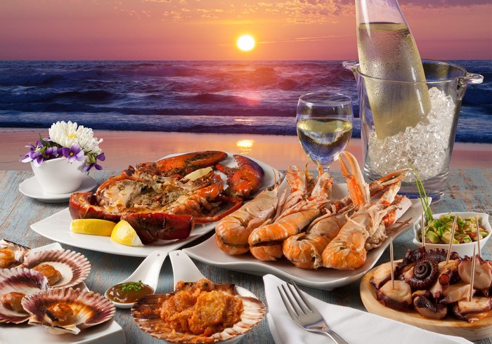 Seafood platter with lobster and wine by the ocean at sunset