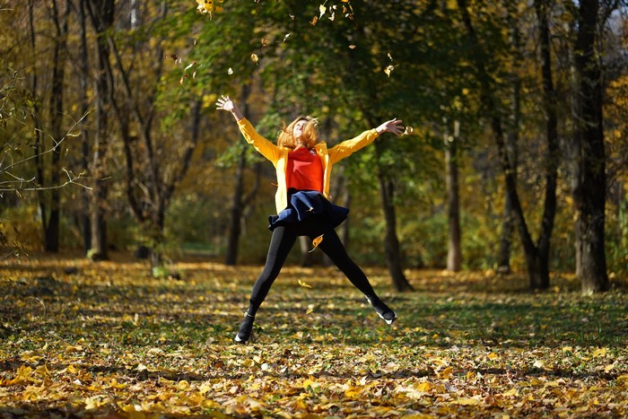 Woman jumping in autumn park with falling leaves