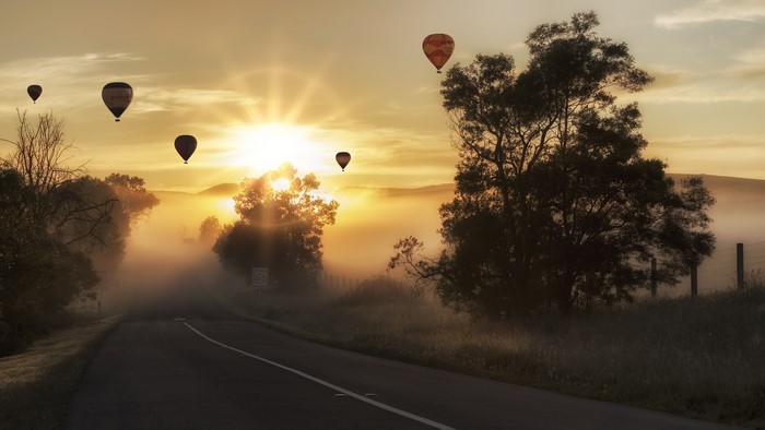 Hot air balloons over a foggy road at sunrise