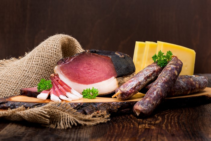 Meat products, ham, sausage, and cheese on a wooden board