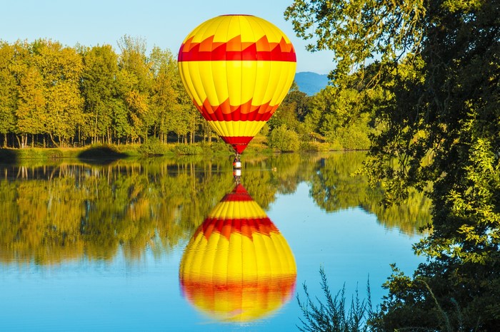 Hot air balloon reflected in a lake with trees