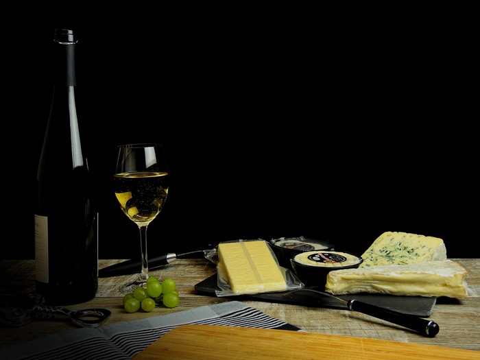 Wine bottle, glass of wine, cheese, and grapes on a table