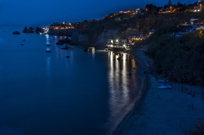 Night view of a coastal town with illuminated buildings and the sea
