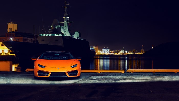 Orange Lamborghini Huracan parked at night by a ship