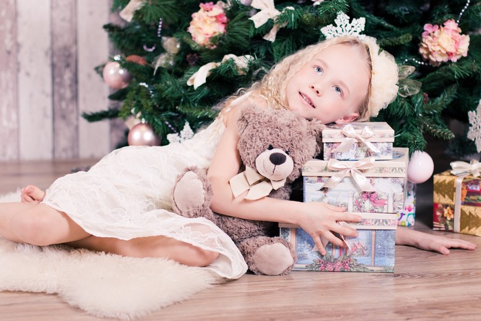 Girl with teddy bear and gifts near Christmas tree